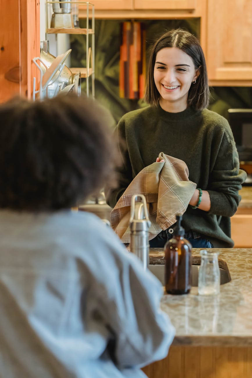 young happy woman drying dishes with towel while listening to friend